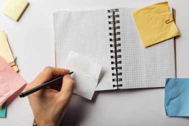 cropped view of man writing on sticky note near opened notebook  clipart
