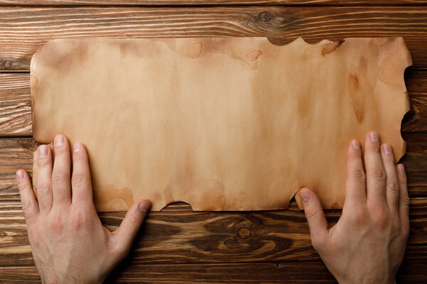 top view of man holding hands near aged parchment sheet