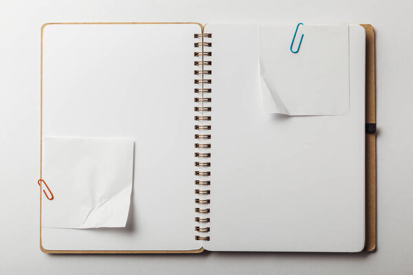 top view of opened notebook with sticky notes and paper clips on white background