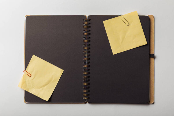 top view of opened notebook with black sheets and sticky notes with paper clips on white background