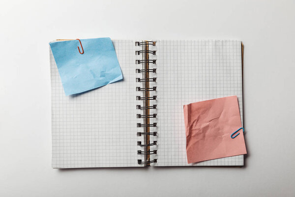 top view of opened notebook with squared papers and crumpled blue and pink sticky notes on white background