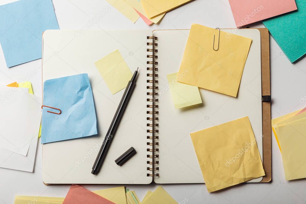 top view of opened notebook with sticky notes with paper clips and black pen on white background