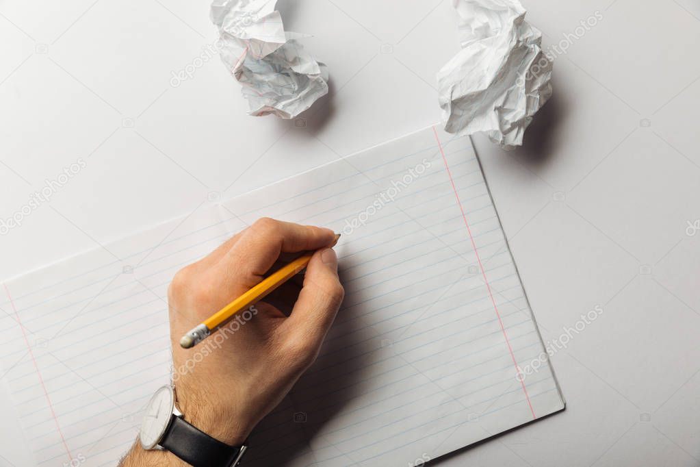 cropped view of man holding pencil near lined sheet and crumpled papers on white background 