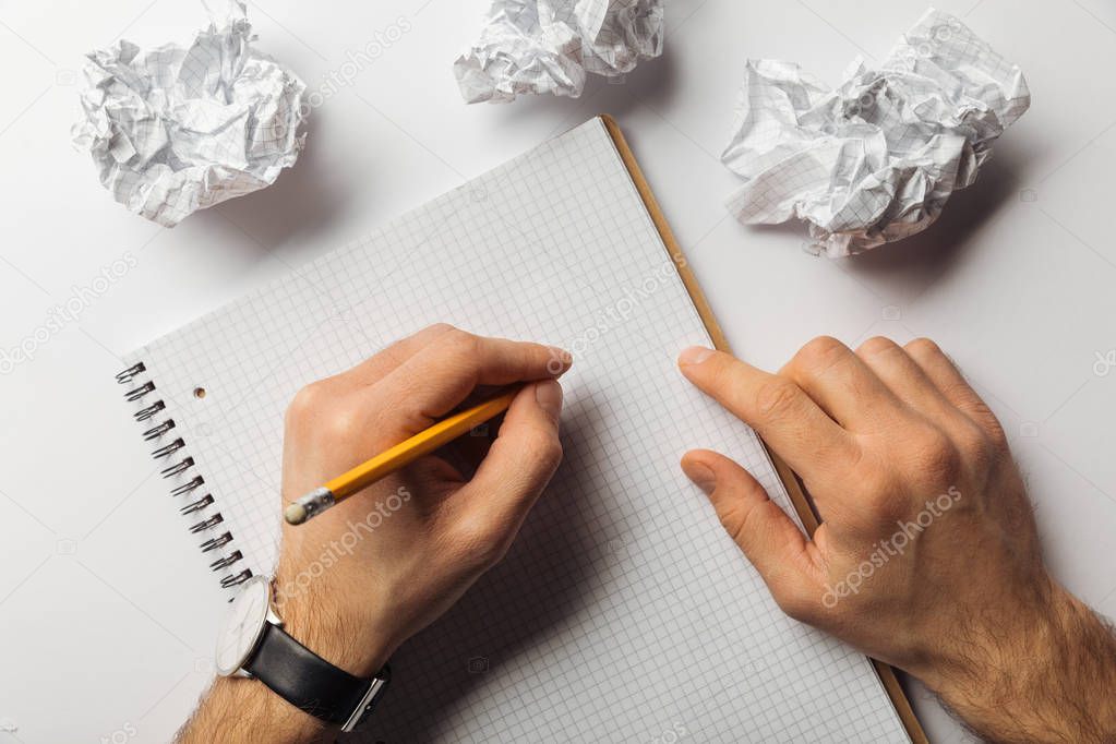 cropped view of man writing on blank squared sheet near crumpled papers on white background 