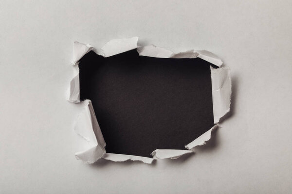 torn hole in sheet of paper on black background