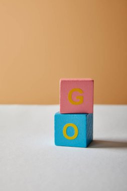vertical go lettering made of multicolored blocks on white table and beige background clipart