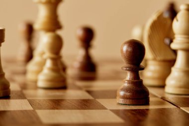selective focus of pawn piece on wooden brown chess board and beige background clipart