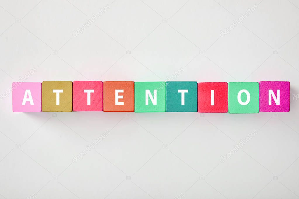 top view of attention lettering made of multicolored cubes on grey background