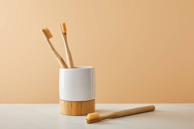 Bambu diş fırçası ve tutucu beyaz masa ve bej renkli arka plan üzerinde
