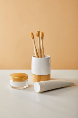 Bambu diş fırçası tutucu, diş macunu tüpü ve beyaz masa ve bej renkli arka plan üzerinde kozmetik krem