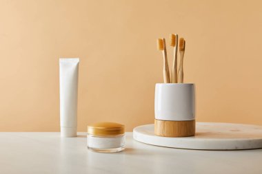 mermer üzerinde bambu diş fırçası ile beyaz sahibi yuvarlak masa, diş macunu tüpü ve tablo ve bej renkli arka plan üzerinde kozmetik krem