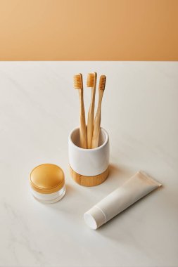 Bambu diş fırçası, diş macunu tüpü ve beyaz mermer masa ve bej renkli arka plan üzerinde kozmetik krem ile sahibi