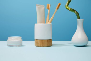 diş fırçası, kozmetik krem ve tablo ve mavi arka plan bambu kök için tutucu