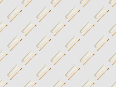 diagonally located bamboo toothbrushes and toothpaste in tubes on grey background, seamless background pattern clipart