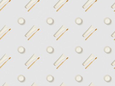 diagonally located bamboo toothbrushes, toothpaste in tubes and cosmetic cream on grey background, seamless background pattern clipart