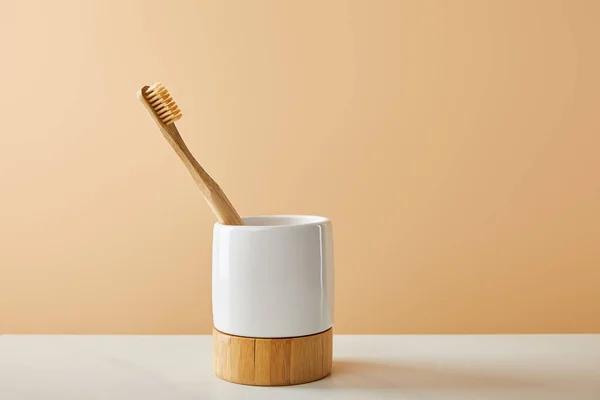 白いテーブルとベージュ色の背景上のホルダーに竹の歯ブラシ — ストック写真