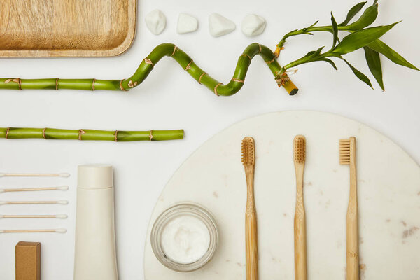 top view of ear sticks, toothpaste in tube, cosmetic cream, toothbrushes and bamboo stems on white background