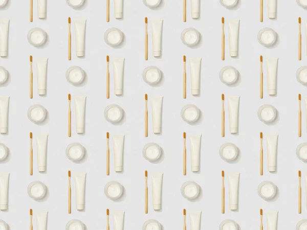 vertically bamboo toothbrushes, toothpaste in tube and cosmetic cream on grey background, seamless background pattern