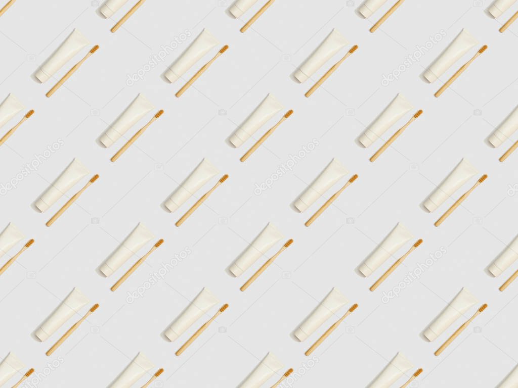 diagonally located bamboo toothbrushes and toothpaste in tubes on grey background, seamless background pattern
