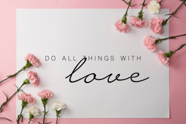 top view of pink and white carnation flowers and card with do all things with love lettering on pink background clipart