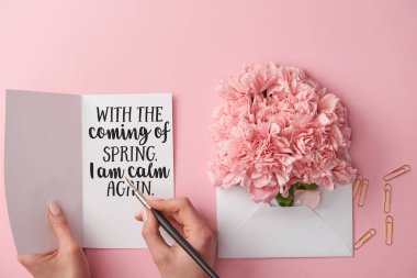 Zarfın üzerinde pembe bir arka plan bahar tebrik kartı ve karanfil çiçek kalemin tutan kadının kırpılmış görünümü