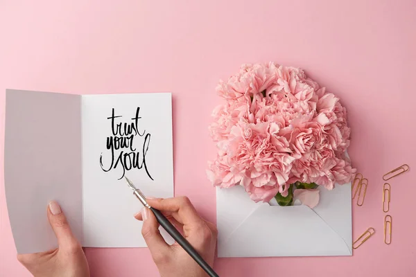 裁剪的妇女拿着贺卡的景象与信任你的灵魂字母和笔附近康乃馨花在信封在粉红色的背景 — 图库照片