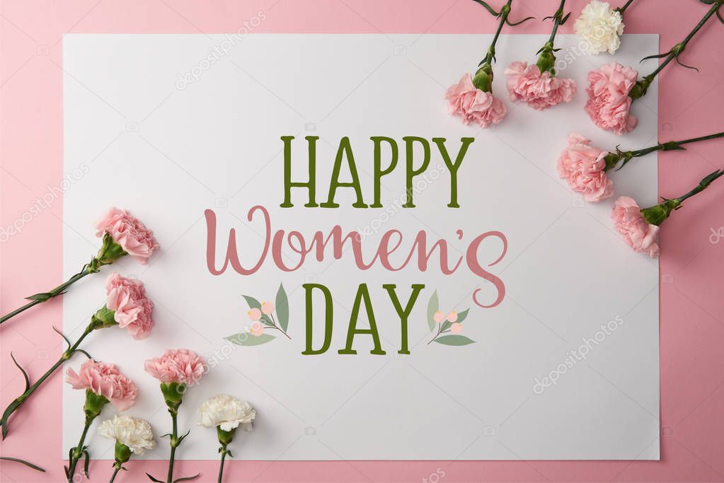 top view of pink and white carnation flowers and greeting card with happy womens day lettering on pink background