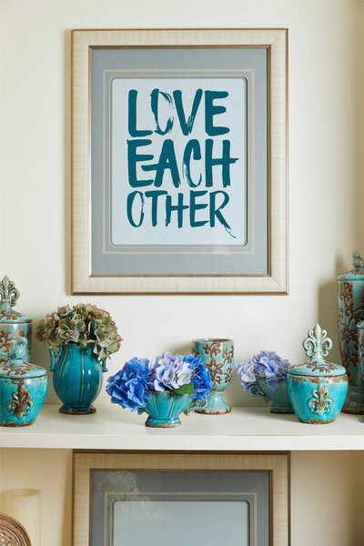 picture frame with love each other lettering and turquoise ceramic ornate vintage vases with flowers on shelf