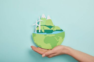 top view of woman holding paper cut planet with renewable energy sources on turquoise background, earth day concept clipart