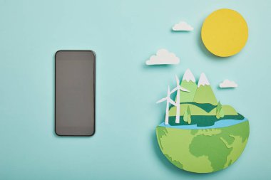 top view of blank screen smartphone and paper cut planet with renewable energy sources on turquoise background, earth day concept clipart