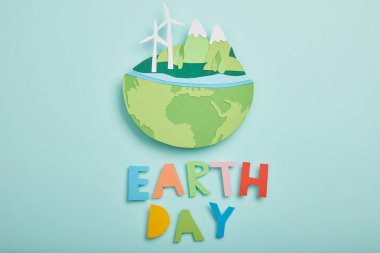 top view of paper cut planet with renewable energy sources and colorful paper letters on turquoise background, earth day concept clipart