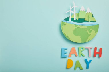 top view of paper cut planet with renewable energy sources and colorful letters on turquoise background, earth day concept clipart
