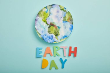 top view of colorful paper letters and planet picture on turquoise background, earth day concept clipart