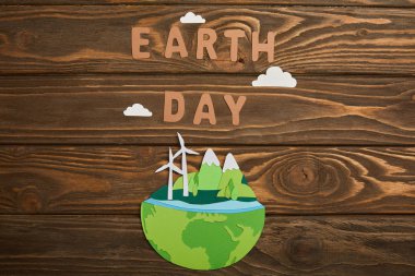 top view of paper cut planet with renewable energy sources and paper letters on wooden background, earth day concept clipart