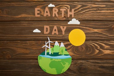 top view of paper cut planet with renewable energy sources and letters on wooden background, earth day concept clipart