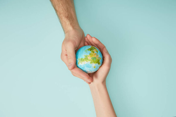 вид сверху на мужчину и женщину, держащих модель планеты на бирюзовом фоне, концепция Дня Земли
