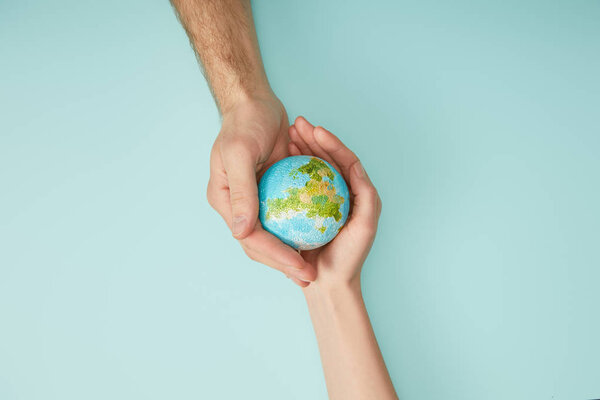 top view of man and woman holding planet model on turquoise background, earth day concept