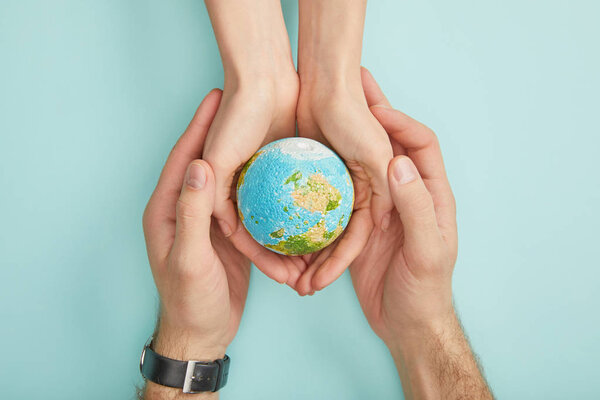 top view of man and woman holding planet model on turquoise background, earth day concept