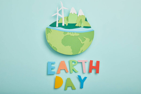 top view of paper cut planet with renewable energy sources and colorful paper letters on turquoise background, earth day concept