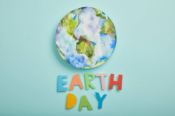 top view of colorful paper letters and planet picture on turquoise background, earth day concept