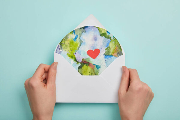 top view of woman holding envelope with planet picture on turquoise background, earth day concept