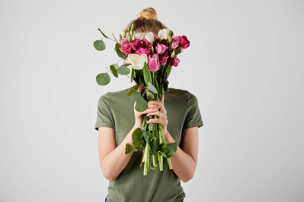 girl holding bouquet with tulips, eucalyptus and roses in front of face isolated on grey with copy space