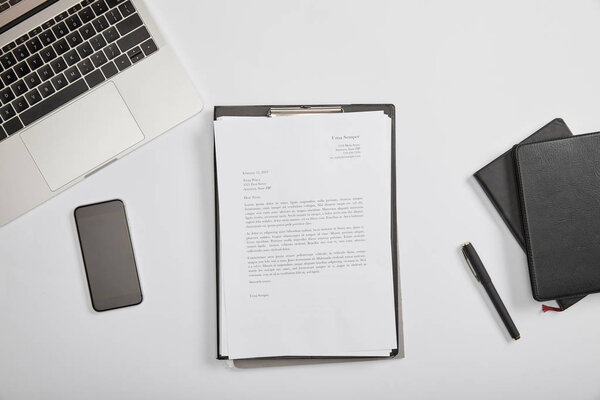 top view of documet on clipboard, smartphone, pen, laptop and notebooks 