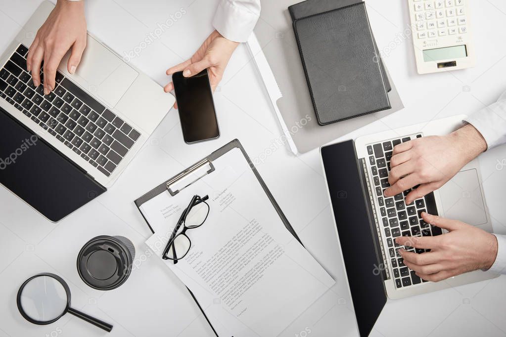 top view of businesspeople typing on laptops and holding smartphone 