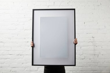 woman covering face while standing and holding blank black frame  clipart