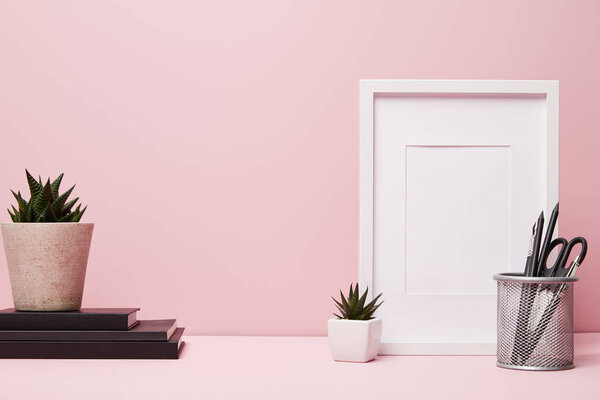 blank frame near green plant, metallic holder with stationery and books