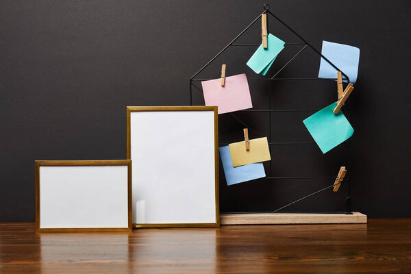 blank frames near metallic holder with sticky notes and pins 