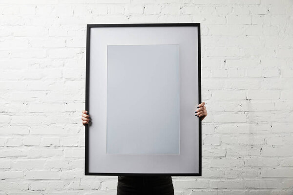 woman covering face while standing and holding blank black frame 