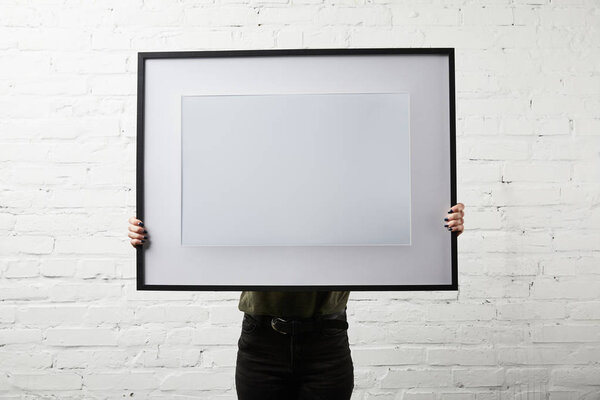 woman covering face while standing and holding blank frame in hands
