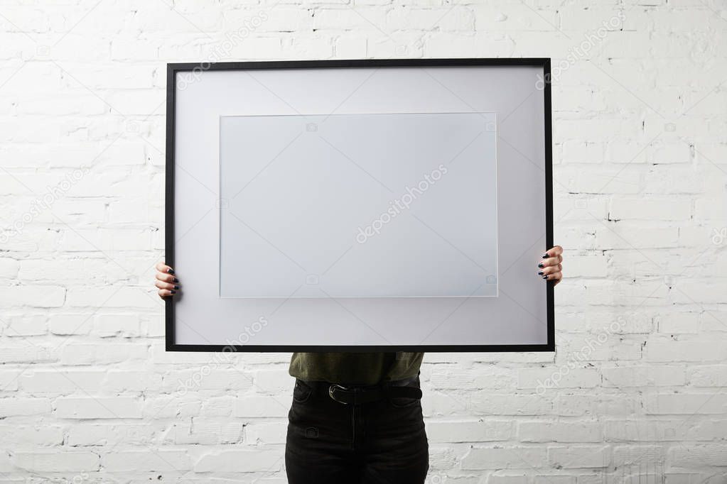 woman covering face while standing and holding blank frame in hands